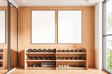 Dambıl üzerindeki ahşap duvarda asılı iki boş poster modern bir spor salonunun içinde, doğal ışıklandırma ve fitness konseptiyle minimalist tarzda. 3B Hazırlama