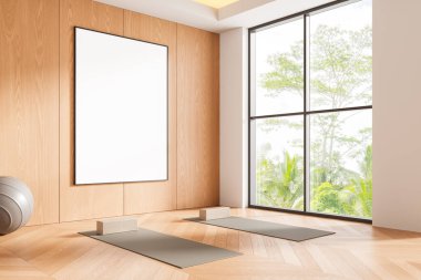 Minimalist yoga odasında ahşap bir duvarda büyük boş bir poster, temiz ve parlak üç boyutlu iç mekan büyük pencereli ve gür ağaçlar var.