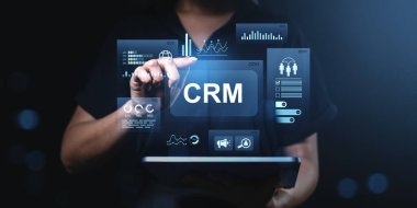 Veri analizi ve iletişim simgeleriyle CRM arayüzü kullanan kişi, karanlık gradyan arka planda dijital bir şekilde iş teknolojisini sembolize eder.