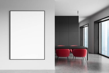 Modern iç mekandaki temiz beyaz duvara asılı boş çerçeveli poster modeli, kırmızı sandalyeler ve karanlık tasarımla dolu ofis alanının yanında. 3B Hazırlama