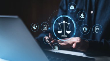 Adalet ölçeği hologramı ve yasal ikonlar, dijital hukuk ve hukuki teknolojiyi sembolize eden karanlık bir arkaplanda, bir insanın elinin üzerinde asılı duruyor.