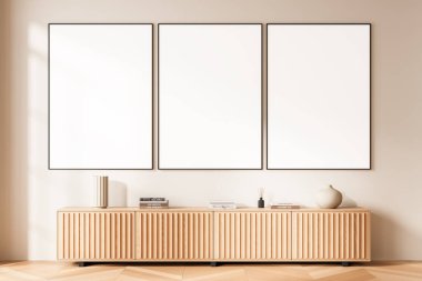 Ahşap bir dolabın üstündeki temiz bej bir duvara asılmış üç boş poster modeli ve parlak minimalist iç dekorasyon ürünleri. 3B Hazırlama