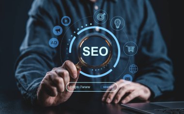 Koyu arkaplanda dijital pazarlama simgeleri olan SEO metni üzerinde büyüteç tutan bir kişi, çevrimiçi arama optimizasyon stratejisini sembolize ediyor