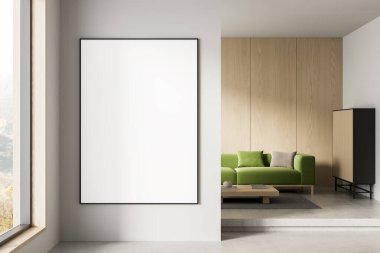 Modern bir iç mekanın temiz beyaz duvarında boş bir poster modeli, ahşap panelli minimalist tasarım ve arka planda yeşil kanepe. 3B Hazırlama