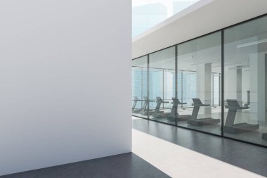 Zeminden tavana cam duvarlar, minimalist mimari, şehir manzarası arka planı, kentsel fitness kavramı arkasında modern bir spor salonunda koşu bandı. 3B Hazırlama