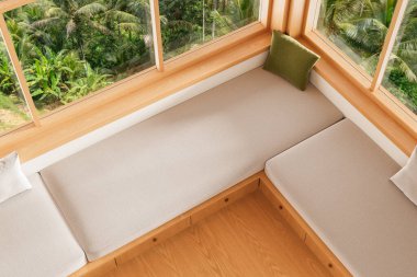 Sıcak, ahşap döşeme döşemeleri ve yeşil yastıklı, büyük pencerelerle çevrili, dışarıda tropikal ormanlar olan köşedeki bank. 3B Hazırlama