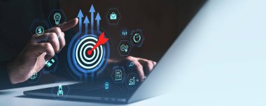 Kişi, dijital hedef sembolü ve iş simgeleri ile fütüristik grafik tarzında, karanlık bir arkaplanda, iş stratejisi kavramını temsil eden etkileşim halindedir.