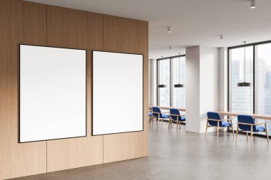 Modern ofis içi aydınlık ahşap duvarda iki boş poster. Mavi sandalyeli, büyük pencereli ve beton zeminli temiz bir tasarım. 3B Hazırlama