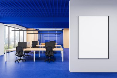 Mavi döşemeli ve tavanlı modern ofis, ahşap masalar, bilgisayar çalışma istasyonları, ve beyaz bir duvarda boş bir poster modeli. 3B Hazırlama