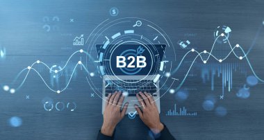 Bilgisayarda B2B simgesi ve dijital iş grafikleriyle ahşap masa arkaplanı üzerinde yazı yazan eller, iş stratejisini ve veri analizini sembolize ediyor