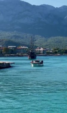 Bir tekne, dağların arka planına karşı kıyıya doğru yelken açar.