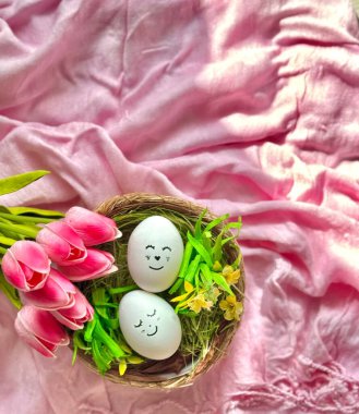 Yüzleri boyalı iki yumurta pembe kumaş ve pembe lalelerin arasında bir yuvada yatıyor.