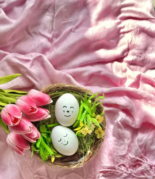 Yüzleri boyalı iki yumurta pembe kumaş ve pembe lalelerin arasında bir yuvada yatıyor.