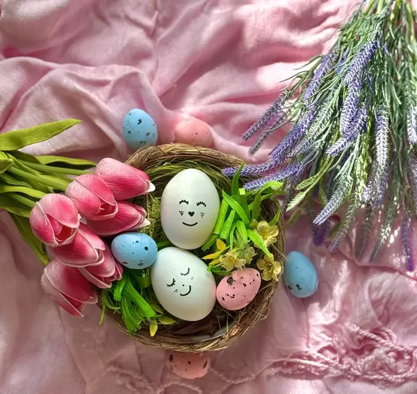 Dekoratif bir yuvada çok renkli Paskalya yumurtaları ve iki buket çiçek.