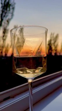 Gün batımının ılık renklerini yansıtan bir şarap kadehinin yakın çekimi, narin su damlacıkları güzel yansımalar yaratıyor..