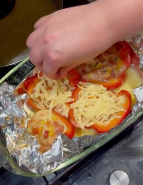 Kırmızı çan biberlerinin üzerine dilimlenmiş peynir serpiştiren bir el lezzetli bir mısır ve etle doldurulmuş, folyo kaplı cam bir fırın tabağına konmuş, fırın için hazır..