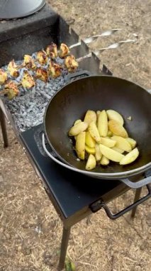 Baharatlı patates dilimleriyle dolu dökme demir bir tencere parlayan kömür üzerinde kaynarken bükülmüş metal et şişleri yukarıda engebeli bir açık hava ortamında pişiyor..