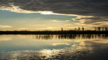 dramatik, zıt gökyüzü gölün yüzeyindeki yansımalarla ufuktaki karanlık ağaç siluetleri, sonbahar