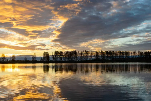 stock image Beautiful lake at sunrise, golden hour sunrise, sunlight and grand cloud reflections on water, colorful dramatic sky at sunrise, dark silhouettes of trees, motion blur