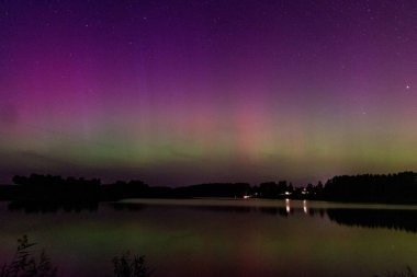 Aurora Borealis 'in devasa, çok renkli yeşil görüntüsü. Aurora Polaris, Letonya' da bir gölün üzerinde gece gökyüzünde kuzey ışıkları olarak da bilinir.