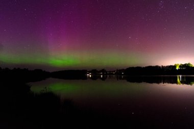 Aurora Borealis 'in devasa, çok renkli yeşil görüntüsü. Aurora Polaris, Letonya' da bir gölün üzerinde gece gökyüzünde kuzey ışıkları olarak da bilinir.
