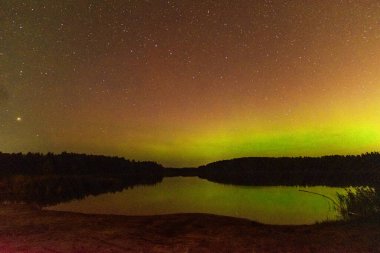 Aurora Borealis 'in devasa, çok renkli yeşil görüntüsü. Aurora Polaris, Letonya' da bir gölün üzerinde gece gökyüzünde kuzey ışıkları olarak da bilinir.