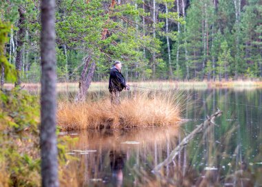 Bataklık gölü, orman ve bataklık bitkisinin kıyısında bir balıkçı, yağmurlu ve bulutlu bir sonbahar günü