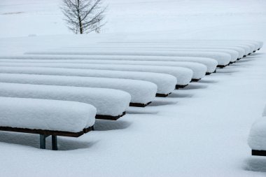 Beyaz kış günü, kalın bir kar örtüsüyle kaplı ahşap banklar, ışık ve gölge oyunları, ritim
