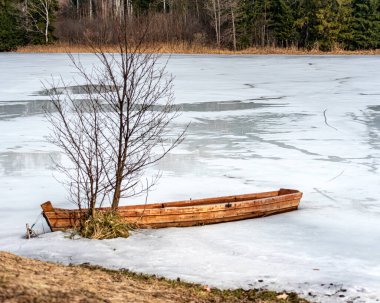 Buzun içinde donmuş ahşap bir kayıkla bahar manzarası gölün kıyısında terk edilmiş tekneler, kışın sonları, doğanın ilk baharları.