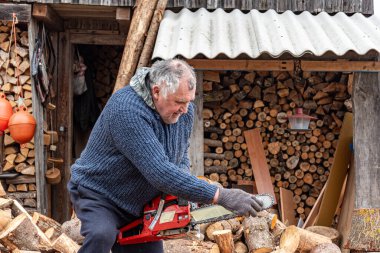 Bir adam testereyle çalışıyor, kış mevsimi için yakacak odun işliyor, kırsal kesimde odun ısıtıyor.