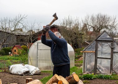 Bahçesinde baltayla çalışan bir adam kış mevsimi için yakacak odun, yakacak odun ve yakacak odun işliyor.