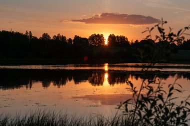 Renkli gün doğumu, göl kenarındaki günbatımı manzarası, parlak renkli gökyüzü gölün suyuna yansıyor, Mazais Ansis, Rubene, Letonya