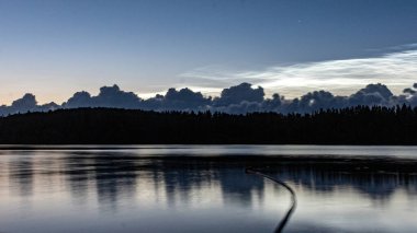 charming night landscape with silver clouds, silver clouds over the lake, dark forest silhouette in the background, mesospheric clouds, Latvia, Lake Vaidava clipart