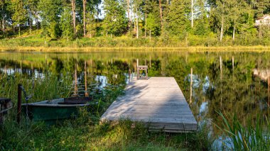 Küçük bir orman gölü, gölün kıyısında bir tekne, akşam ışığında saf bir göl, sakin bir yaz akşamı.