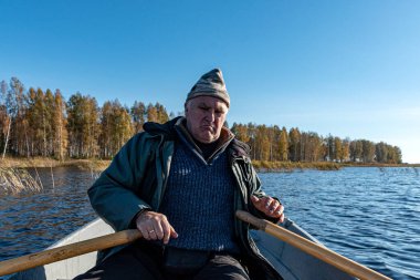 Bir teknedeki balıkçı, gölün kıyısındaki ağaçların renkli arka planı, sonbahar.