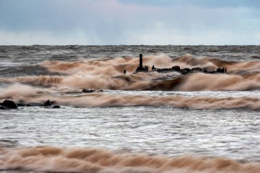 dramatic storm in the Baltic Sea, large waves crashing against the stone pier, blurred, unclear contours, rocky shore of Vidzeme, Thuja, Latvia clipart