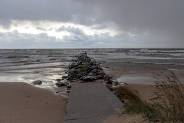 dramatic storm in the Baltic Sea, large waves crashing against the stone pier, blurred, unclear contours, rocky shore of Vidzeme, Thuja, Latvia clipart