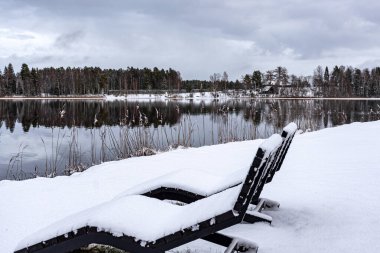 Sakin gölü olan kış manzarası, göl kıyısında karla kaplı şezlong, doğada büyüleyici bir huzur, Vaidava Gölü, Letonya, kış