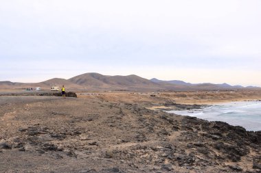 El Cotillo, Fuerteventura, Kanarya Adaları, İspanya - 21 Kasım 2023: İnsanlar bulutlu bir günde kayalık bir sahil şeridiyle baş döndürücü bir sahilin keyfini çıkarıyorlar.
