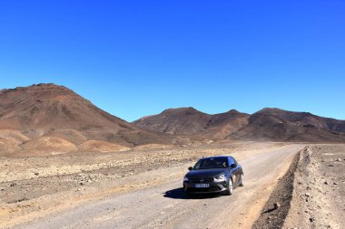 19 Kasım 2023 - Morro Jable, Jandia, Fuerteventura İspanya 'da: Arka planda yüksek volkanik dağları olan çakıllı, tozlu yol