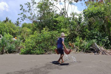 Kuşamba, Endonezya 'dan Bali - 08 Şubat 2024: Denizdeki suyu toplayan çiftçi, buharlaşma için tuz tarlasına gitti