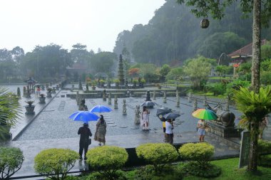 Bali, Endonezya - Şubat 05 2024: İnsanlar yağmurlu bir günde Doğu Bali 'deki Tirta Gangga Su Sarayı' nın tadını çıkarıyor