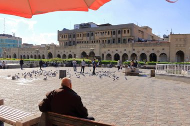 Erbil, Erbil, Kürdistan, Irak - 20 Kasım 2024: Şehir merkezindeki Şah Parkı 'nda saat kulesinin yanında dinlenen insanlar, Parki Sar