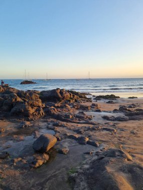 Huzurlu bir Tenerife sahili. Okyanusta tekneler, kayalık kıyılar ve çarpıcı bir günbatımı var. Sahil şeridinin sakin ve resimli bir manzarası var..