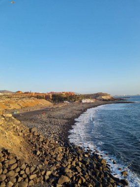 Tenerife 'deki kayalık bir sahilin çarpıcı manzarası. Okyanus, berrak mavi gökyüzünün altında usulca kıyıya vuruyor. Huzurlu ve manzaralı bir kaçış sunuyor..