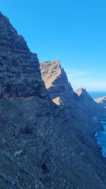 Tenerife 'deki Degollada del Perchel kayalıklarının nefes kesen manzarası, bir tarafında yüksek dağlar ve açık mavi gökyüzünün altına uzanan okyanus..