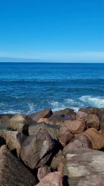 Tenerife 'de sakin bir sahil kıyıları pürüzsüz çakıl taşlarıyla okyanus usulca kıyılara çarpıyor ve yukarıdan uzanan açık mavi gökyüzü sahil şeridini mükemmel bir şekilde görüyor..