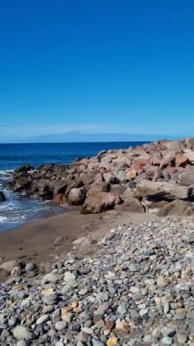 Tenerife 'de sakin bir sahil manzarası, kıyıları saran pürüzsüz çakıl taşları ve açık mavi gökyüzünün altında ufka doğru uzanan engin okyanuslar..