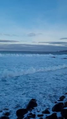 Tenerife 'nin engebeli sahillerinde akşam, dalgalar renkli bir gökyüzünün altında kayalık kıyılara çarpıyor.. 