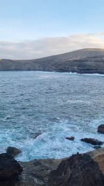 Okyanus dalgalarının kayalık kıyılarla buluştuğu Tenerife sahilinin güzel bir manzarası. Açık mavi gökyüzü plajın doğal güzelliğini arttırır..